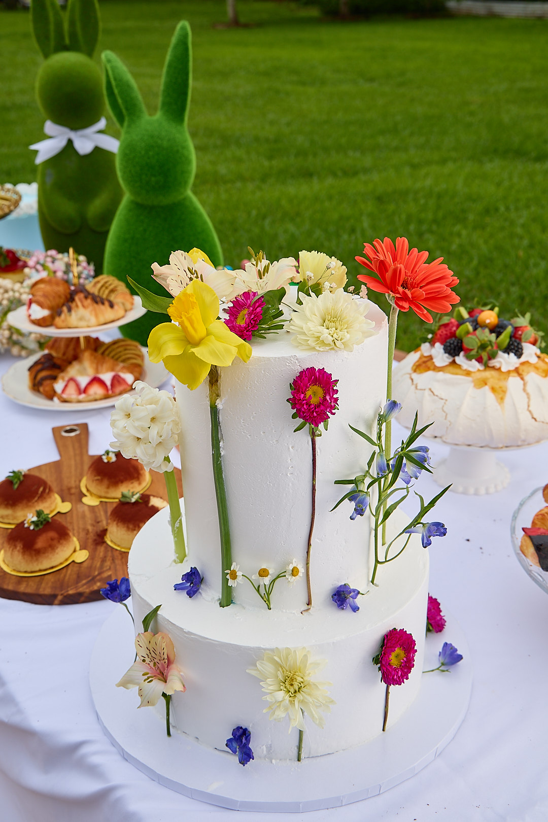 Two-tier floral cake decorated with daffodils, gerbera, and dried flowers, on a spring catering table.