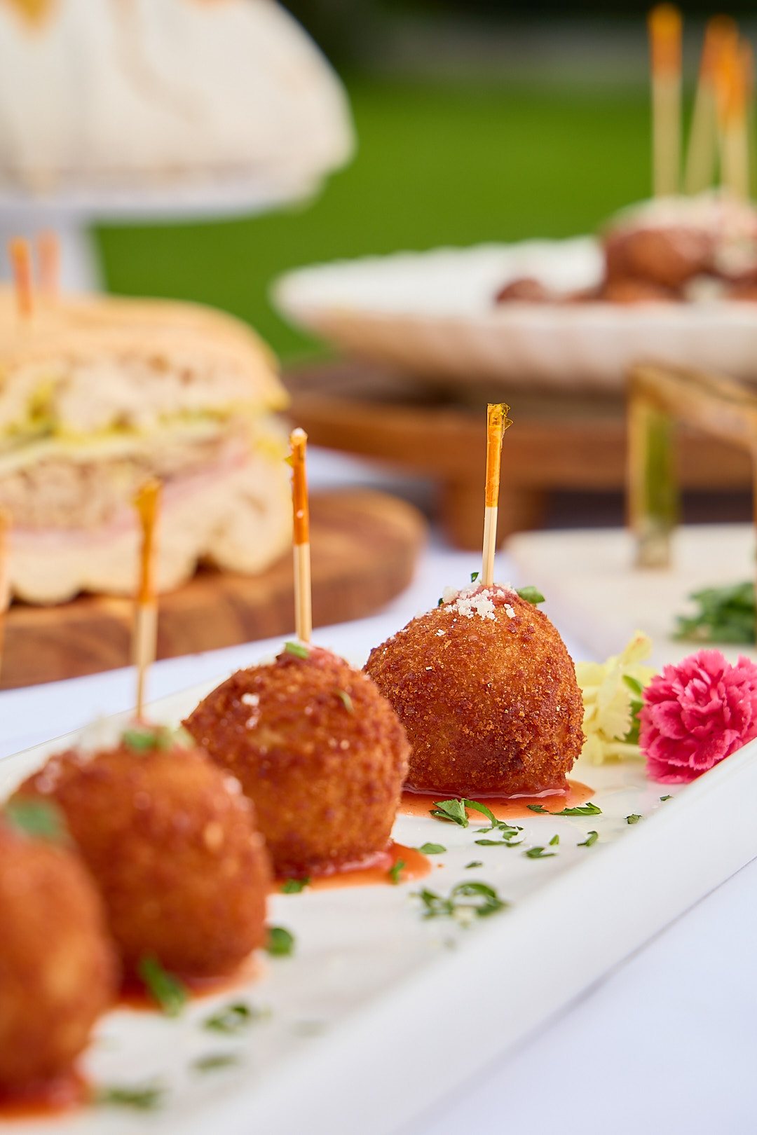Cuban croquettes on a long porcelain plate with red sauce and fresh carnations.