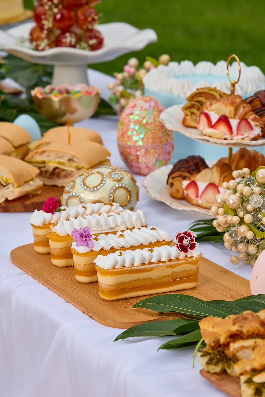 A Dolce Saturno catering board with passionfruit pastries, fresh croissants, sandwich Cubano, and a profiterole tower.