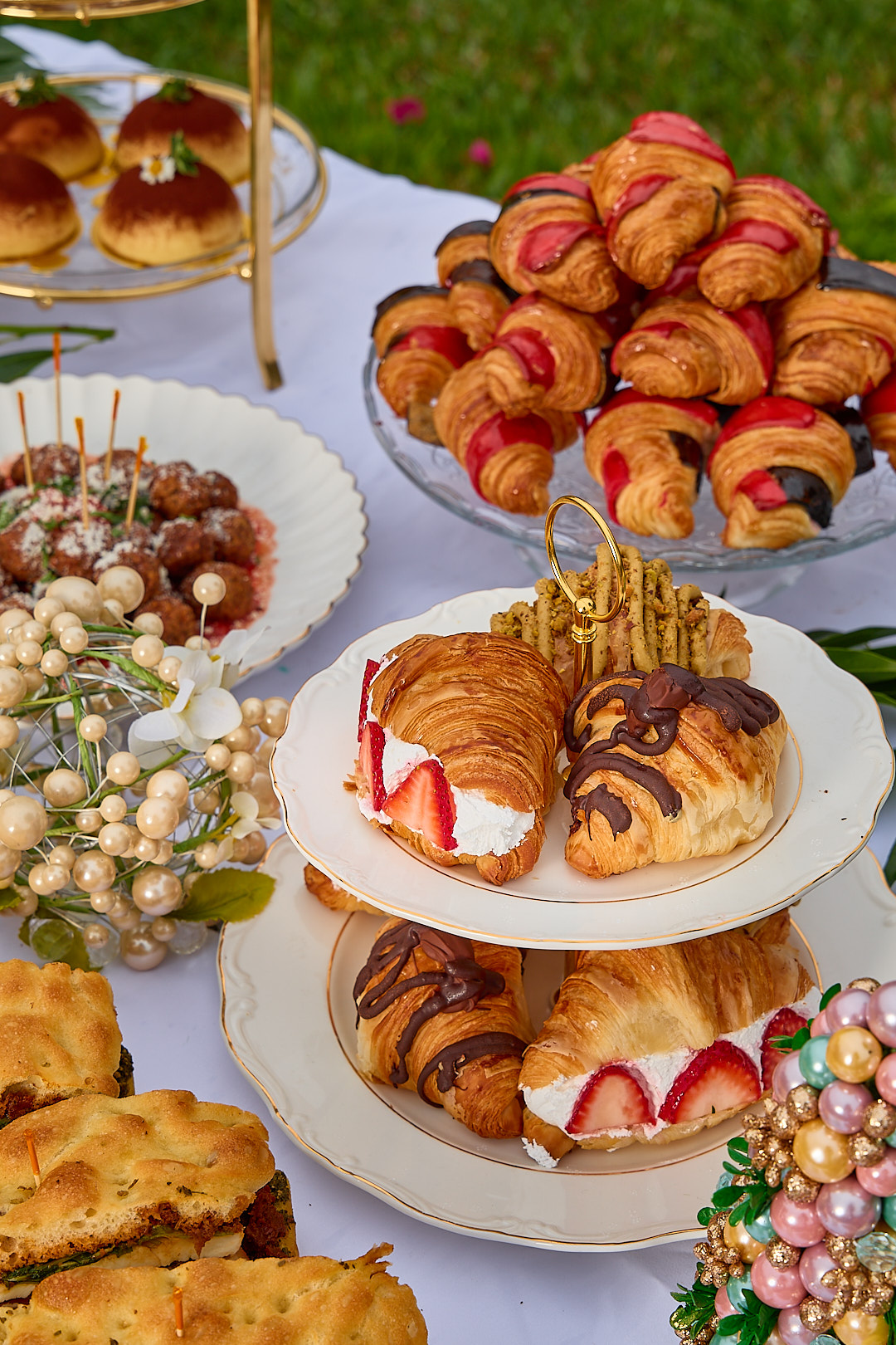 A spread of Dolce Saturno croissants filled with strawberries, chocolate, and pistachio, served on tiered platters in a garden setting.
